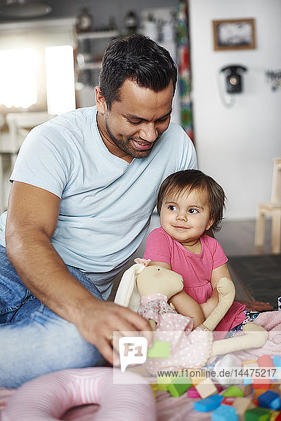 Smiling father and baby girl playing with building blocks at home