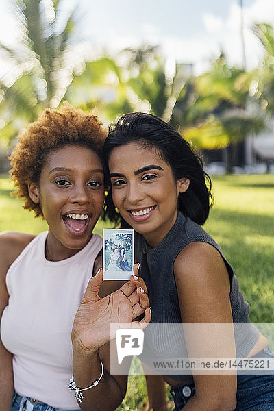 Zwei glückliche Freundinnen zeigen ein Sofortfoto in einem Park