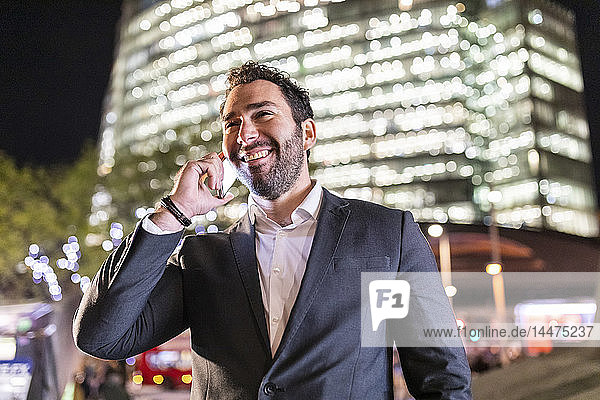 Großbritannien  London  Porträt eines lächelnden Geschäftsmannes  der nachts beim Pendeln telefoniert