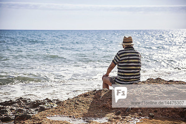 Italien  Sizilien  Cava D'aliga  älterer Mann sitzt an der Küste und schaut auf das Meer