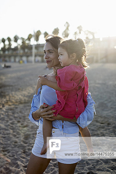 Mutter und Tochter stehen bei Sonnenuntergang am Strand
