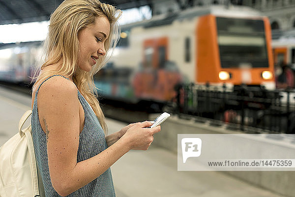 Lächelnde junge Frau benutzt Mobiltelefon am Bahnhof