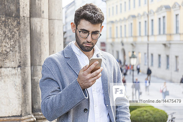 Deutschland  München  Porträt eines jungen Geschäftsmannes  der sein Handy in der Stadt benutzt