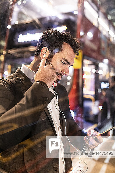Großbritannien  London  Geschäftsmann mit Handy und Ohrstöpseln am Busbahnhof bei Nacht