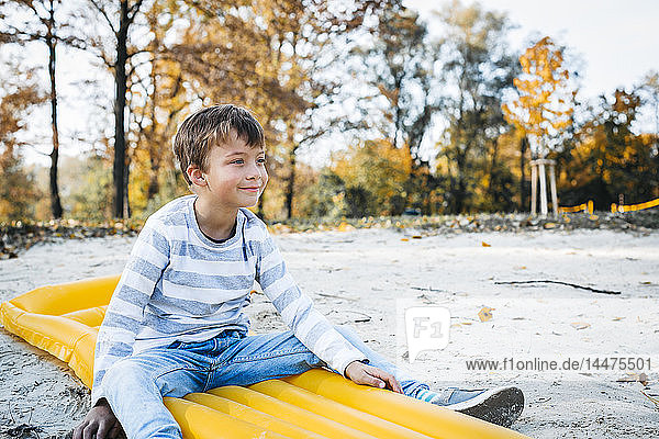 Content little boy sitting on yellow airbed on the beach in autumn