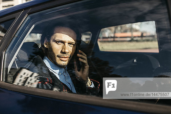 Mann sitzt auf dem Rücksitz eines Autos und telefoniert mit dem Handy