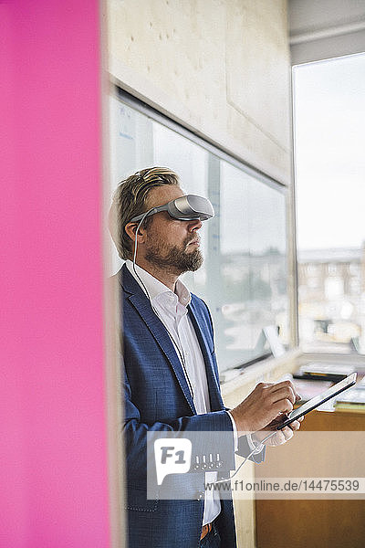 Businessman standing in office  using VR glasses and digital tablet
