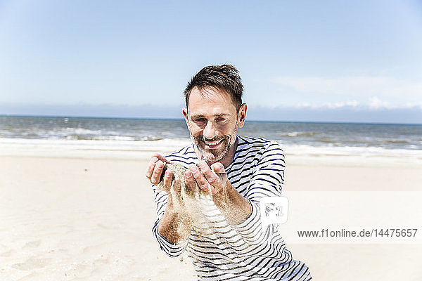 Glücklicher Mann am Strand  der Sand durch seine Hände rieseln lässt