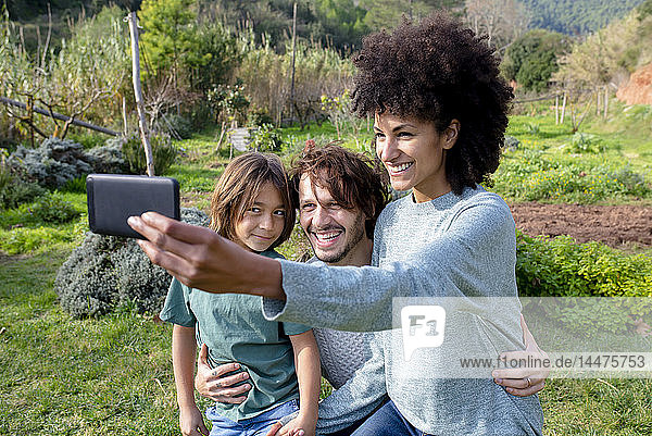 Happy family sitting on a bench in a garden  mother taking selfies