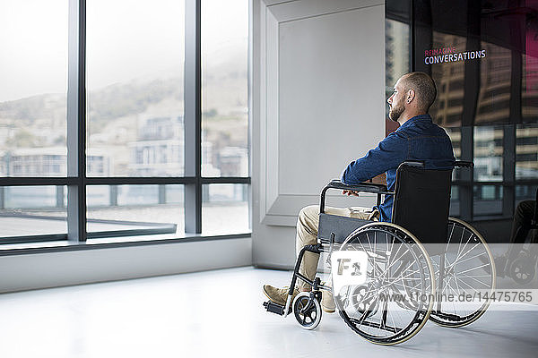 Mann im Rollstuhl schaut im Büro aus dem Fenster