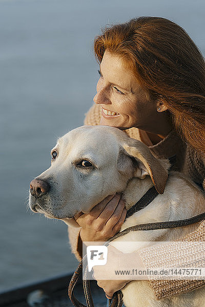 Germany  Hamburg  happy woman cuddling with dog at the Elbe shore