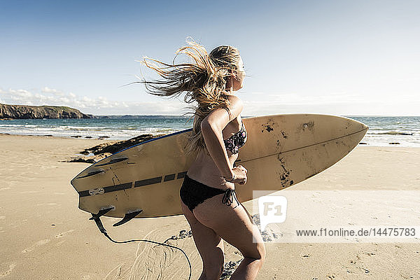 Junge Frau rennt mit einem Surfbrett am Strand