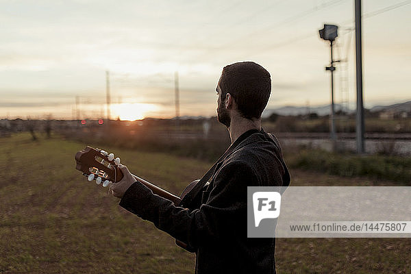 Unbekannter männlicher Musiker spielt Gitarre bei Sonnenuntergang