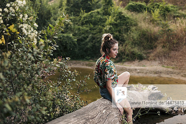 Junge Frau sitzt auf einem Baumstamm inmitten der Natur