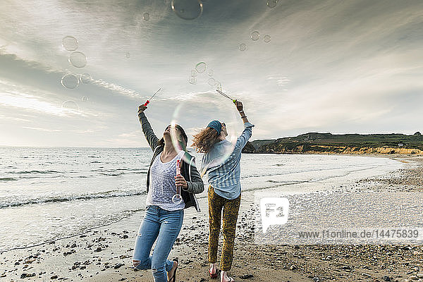 Glückliche Freunde machen Seifenblasen am Strand