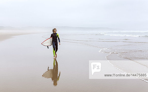 Spanien  Aviles  junger Surfer mit Surfbrett am Strand