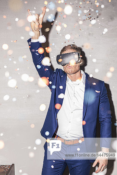 Junger Mann mit Virtual-Reality-Brille steht zwischen Konfettiregen auf einer Party