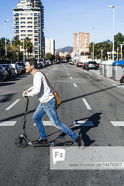 Mature man commuiting in the city with his kick scooter  crossing a street