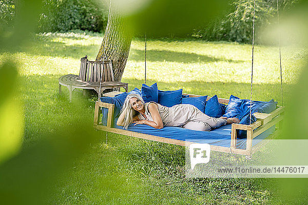 Lächelnde Frau mit langen grauen Haaren liegt auf einem Bett im Garten