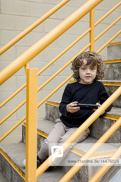 Portrait of boy sitting on stairs with handheld game console