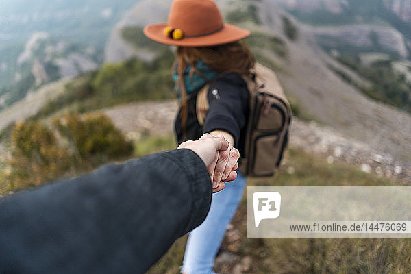 Woman with hat  standing on mountain  holding on to man's hand