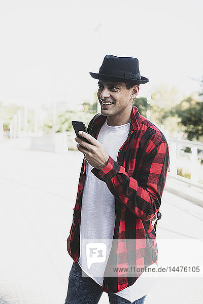 Smiling young man wearing hat and holding cell phone outdoors