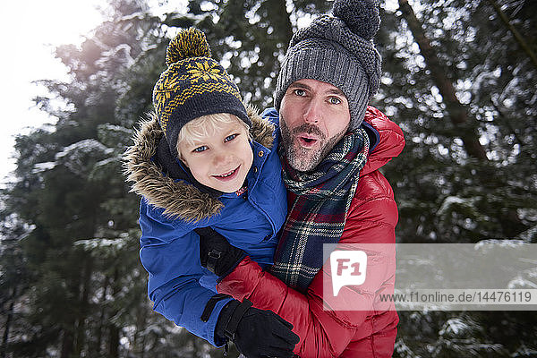 Portrait of father and little son having fun together in winter forest