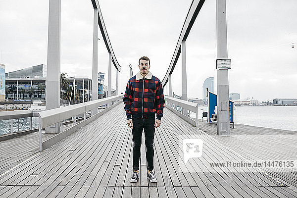 Junger Mann in legerer Kleidung auf einer Hafenbrücke stehend
