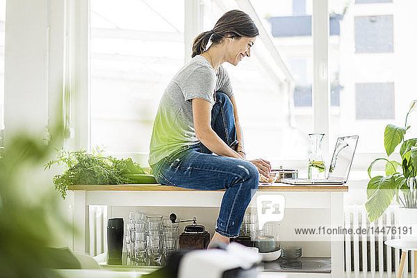 Frau sitzt am Küchentisch  sucht nach gesunden Rezepten  benutzt Laptop