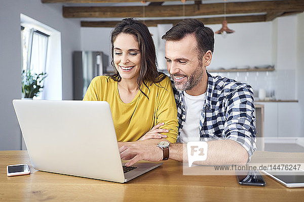Paar sitzt am Esstisch  benutzt Laptop  lächelt