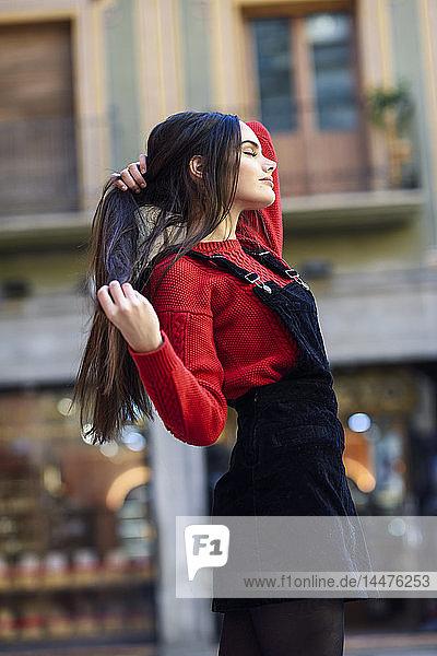 Modische junge Frau mit rotem Strickpullover und schwarzem Trägerkleid in der Stadt