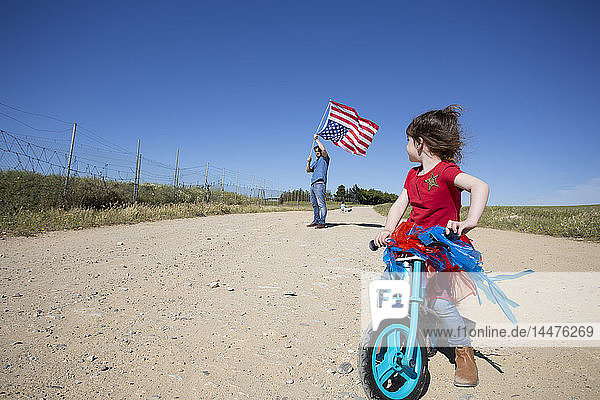 Girl with bicycle and man with American flag on path in remote landscape