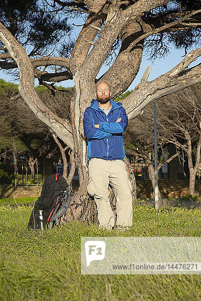Wanderer mit Rucksack während der Wanderung  Anlehnen an Baum  Sonnenbad