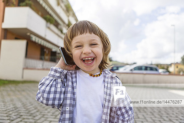 Porträt eines lachenden Kleinkindes mit Handy im Freien