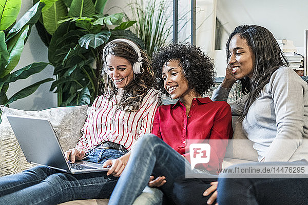 Three happy women with laptop sitting on couch