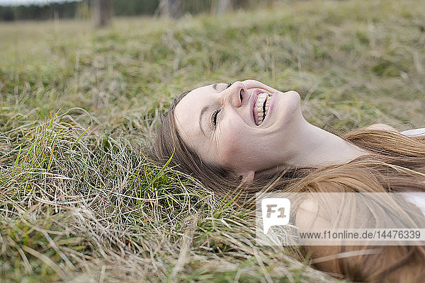 Lachende junge Frau liegt auf einer Wiese