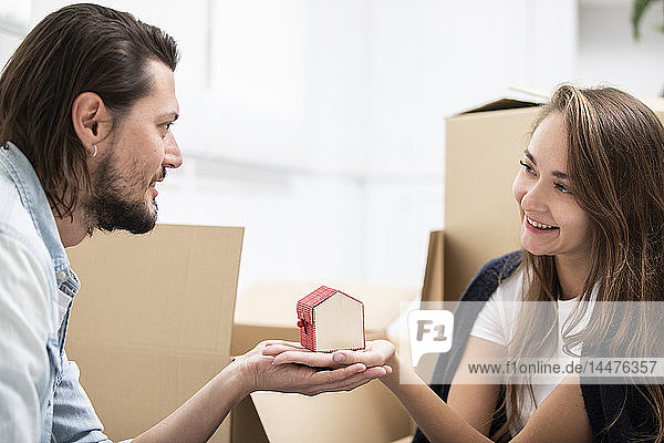Mann übergibt winziges Hausmodell an Freundin  umgeben von Pappkartons