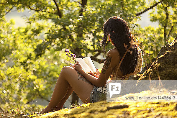 Young woman in forest holding flowers reading a book