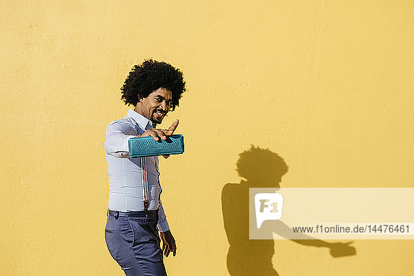 Lächelnder Mann mit Lautsprecher  der Musik hört und vor der gelben Wand tanzt