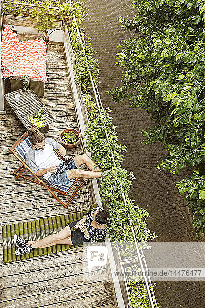 Junges Paar entspannt sich im Sommer auf ihrem Balkon  Mann benutzt Tablette