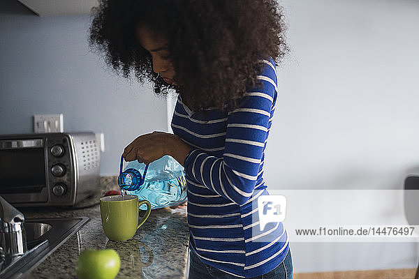Junge Frau gießt Wasser in einen Becher in ihrer Küche