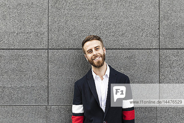 Portrait of smiling stylish businessman in front of grey wall
