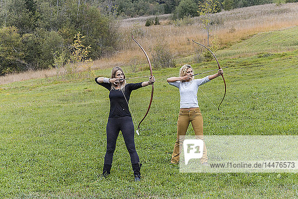 Two archeress standing on a meadow aiming with her bows