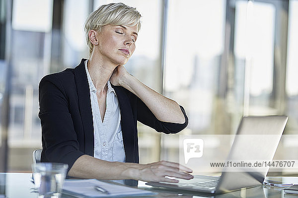 Erschöpfte Geschäftsfrau sitzt mit geschlossenen Augen am Schreibtisch im Büro