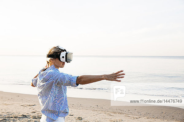 Blonde woman doing kind of yoga exercises on a beach in thailand with 3D virtual reality goggles