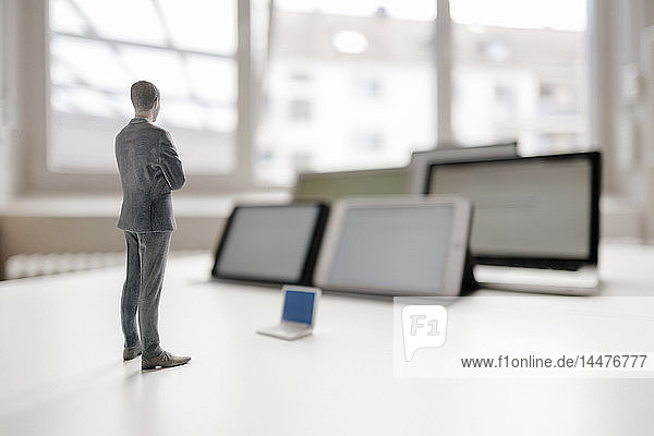 Geschäftsmann-Figur auf Schreibtisch stehend  mobilen Geräten zugewandt