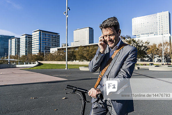 Mature businessman commuting in the city with his kick scooter  usine smartphone