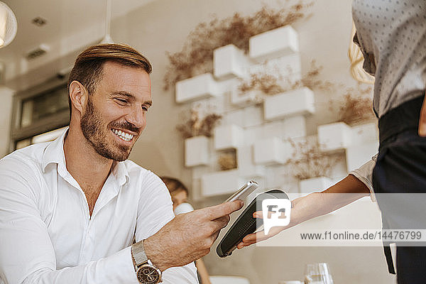 Smiling man paying with smart phone in cafe
