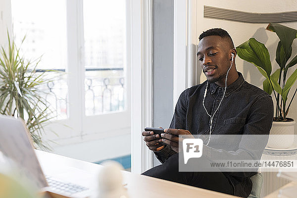 Porträt eines jungen Geschäftsmannes mit Smartphone und Kopfhörern im Büro