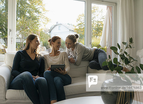 Glückliche Mutter mit zwei Mädchen im Teenageralter  die zu Hause Tabletten auf der Couch benutzen